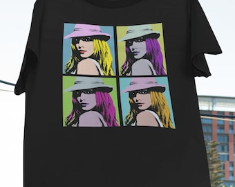 May include: Black t-shirt with a pop art design featuring four images of a woman wearing a hat. The woman's hair is yellow, purple, and blonde. The background is a grid of colorful squares.