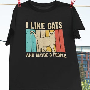 May include: Black t-shirt with a vintage-style graphic of a cat and the text "I like cats and maybe 3 people".