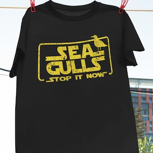 May include: Black t-shirt with a yellow graphic of a seagull and the text "Seagulls Stop It Now".
