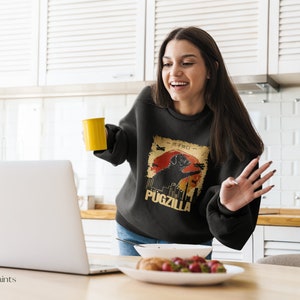 May include: Black sweatshirt with a retro graphic of a pug in front of a cityscape with the text "Pugzilla".