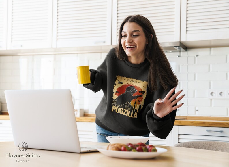 May include: Black sweatshirt with a retro graphic of a pug in front of a cityscape with the text "Pugzilla".
