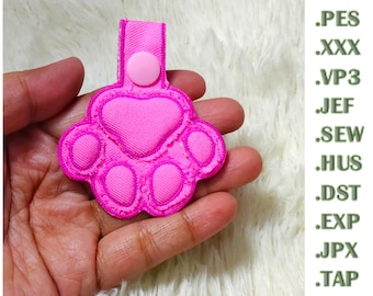 May include: A bright pink embroidered paw print patch with a matching fabric loop and a small pink snap button fastener. The text .PES, .XXX, .VP3, .JEF, .SEW, .HUS, .DST, .EXP, .JPX, and .TAP is listed vertically on the right side of the image.