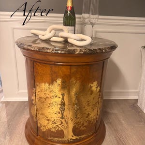 May include: A wooden side table with a marble top, featuring a gold tree design on the front. The table is adorned with a bottle of champagne, two champagne flutes, and a decorative white chain. The word "After" is written in cursive.