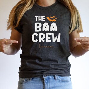 May include: A dark gray t-shirt with the text "The Boo Crew" in white with two white ghosts and orange bats. The name "Lauren" is written in orange below the text.