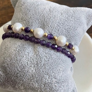 May include: Two bracelets, one with purple amethyst beads and gold spacers, and the other with white pearls and gold spacers.