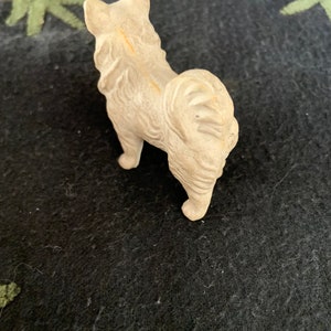 Small plastic Pomeranian figurine. Vintage dog breed collectible. A white LINEOL figurine of a dog standing on a black surface. The dog is facing away from the camera and has its tail curled up.