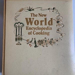 May include: A vintage cookbook titled "The New World Encyclopedia of Cooking." The cover is a light beige with gold lettering and decorative illustrations of kitchenware and birds. The book appears to be in good condition.