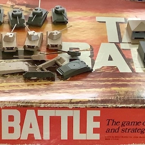 May include: A vintage Tank Battle board game box with game pieces. The box is red and white with the game title in large letters. The game pieces include miniature tanks and buildings.
