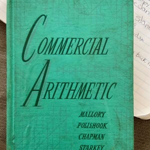 May include: A teal green book titled "COMMERCIAL ARITHMETIC" with the authors' names listed below: Mallory, Polishook, Chapman, Starkey.