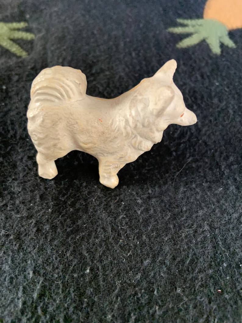 Rare vintage LINEOL Pomeranian figurine. A small white LINEOL figurine of a dog with a fluffy tail. The dog is standing on all four legs and has its head turned to the side.