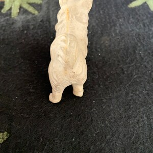 A white LINEOL figurine of a dog standing on a black surface. The dog is facing away from the camera and has a long tail.