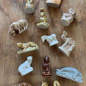 May include: A collection of small ceramic animal figurines in various colors, including brown, tan, white, and gray. The figurines depict a bear, squirrel, leopard, polar bear, and other animals. The figurines are arranged on a wooden surface.