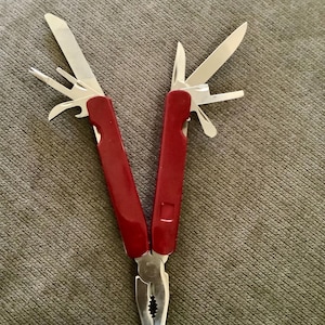 May include: A red and silver multi-tool with various implements, including a knife, screwdriver, and pliers. The tool is open, displaying its different functions. The handles are a vibrant red, contrasting with the silver tools.
