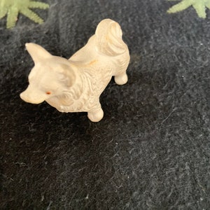 Dollhouse size Pomeranian figure. A small white LINEOL figurine of a dog. The dog is standing on all four legs and has its tail curled up. The figurine is detailed with fur and has a slight sheen.