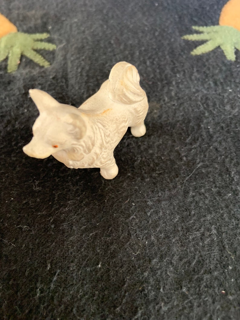 Dollhouse size Pomeranian figure. A small white LINEOL figurine of a dog. The dog is standing on all four legs and has its tail curled up. The figurine is detailed with fur and has a slight sheen.