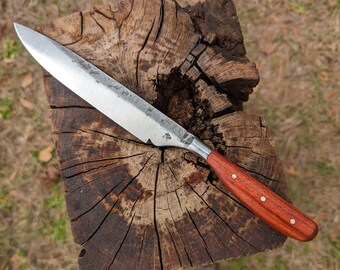 May include: A fixed-blade knife with a silver-colored steel blade featuring a textured finish near the spine and a small clover-shaped stamp. The handle is made of reddish-brown wood secured with three brass rivets, creating a sturdy grip.