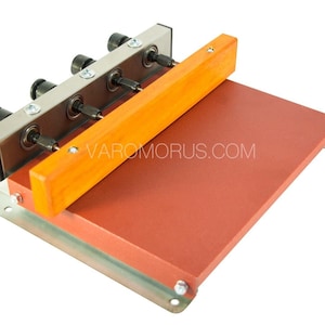 Può includere: Uno strumento in metallo e legno con quattro rulli e una base rossa. Lo strumento è utilizzato per la realizzazione di cinturini in pelle.