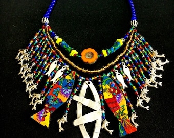 May include: A multi-layered necklace with a blue, gold, and red beaded chain. The necklace features a large silver fish pendant with smaller silver fish charms and colorful fabric fish charms.