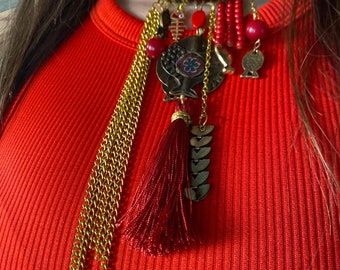 May include: A red and gold statement necklace with a large pendant featuring a fish design. The necklace has multiple chains, beads, and tassels.