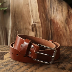 May include: A rolled-up brown leather belt with a silver-colored buckle. The belt has a classic design with a rectangular buckle and a series of holes for adjustment. The leather appears to be of high quality, with a smooth texture and a rich, warm color.