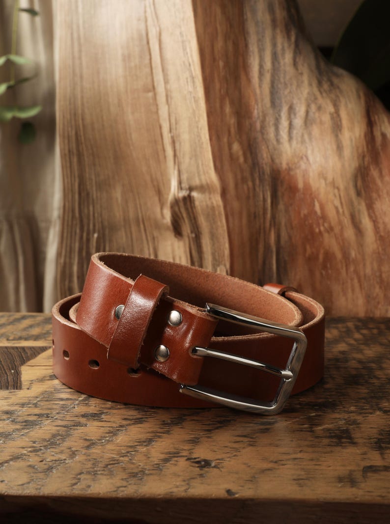May include: A rolled-up brown leather belt with a silver-colored buckle. The belt has a classic design with a rectangular buckle and a series of holes for adjustment. The leather appears to be of high quality, with a smooth texture and a rich, warm color.