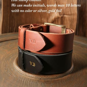 May include: Two leather belts, one brown and one black, stacked on a wooden surface. The brown belt has a gold buckle and the initials "V.B." embossed. The black belt also has "V.B." in gold foil. Text reads "Hot stamp emboss: We can make initials, words max 10 letters with no color or silver, gold foil."