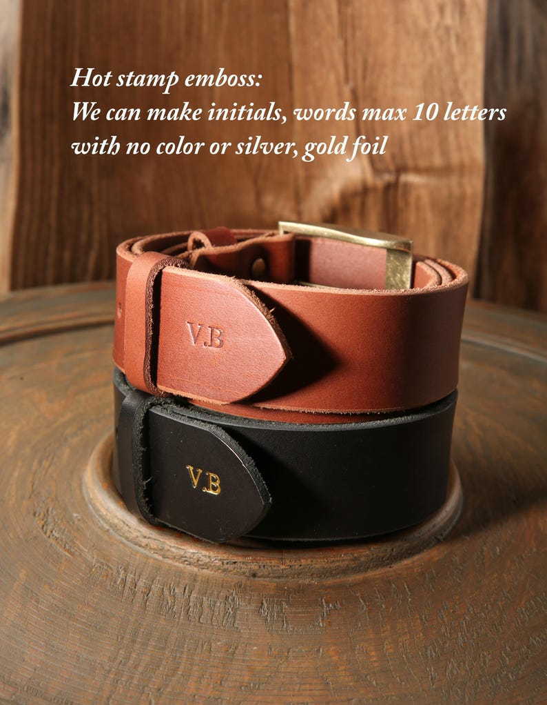 May include: Two leather belts, one brown and one black, stacked on a wooden surface. The brown belt has a gold buckle and the initials "V.B." embossed. The black belt also has "V.B." in gold foil. Text reads "Hot stamp emboss: We can make initials, words max 10 letters with no color or silver, gold foil."