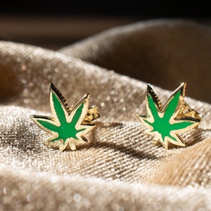 May include: A pair of gold earrings with green enamel marijuana leaf designs.