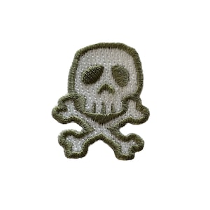 Könnte beinhalten: Ein grüner Stoff-Patch mit einem gestickten weißen Totenkopf und Knochen.