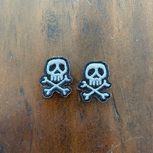 May include: Two small white skull and crossbones patches on a brown wooden surface.