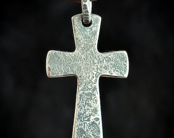 May include: A silver cross pendant with a textured surface. The pendant is attached to a brown leather cord.
