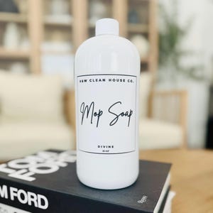 May include: White plastic bottle with a black label that says "H&W Clean House Co. Mop Soap Divine 32 oz."