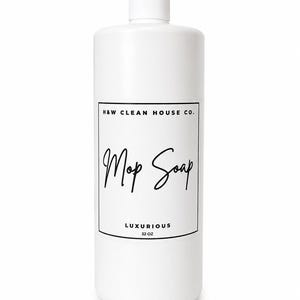 May include: A white plastic bottle with a screw-top cap featuring a rectangular label. The label text reads H&W CLEAN HOUSE CO. at the top, Mop Soap in a script font in the center, and LUXURIOUS 32 OZ at the bottom in black lettering.