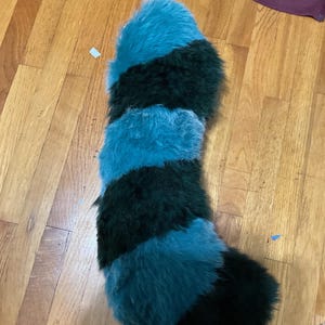 Puede incluir: Una cola larga y esponjosa con rayas alternas de piel azul turquesa y verde oscuro.