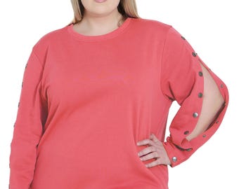 May include: Coral-colored sweatshirt with long sleeves and split sleeves, accented with silver-tone buttons. The casual top features a crew neck and a relaxed fit. The model is wearing black leggings.