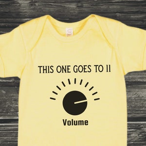 May include: Yellow baby onesie with black text that reads "This one goes to 11" and a black volume knob graphic.