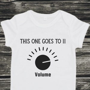 May include: White baby onesie with black text that reads "This one goes to 11" and a black volume knob graphic with the word "Volume" underneath.