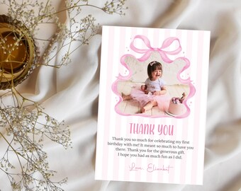 Può includere: Un biglietto di ringraziamento a righe rosa e bianche con la foto di una bambina. La carta presenta un disegno a nastro rosa e le parole "THANK YOU" a lettere grandi. Il testo sulla carta recita: "Grazie mille per aver festeggiato il mio primo compleanno con me!"