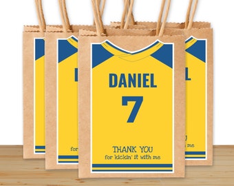 May include: Set of five yellow and blue paper gift bags with a jersey design. The bags have the name "DANIEL" and the number "7" printed on them. The bags have a thank you message that reads "THANK YOU for kickin' it with me".