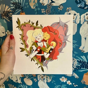 May include: Square art print featuring two cartoon women embracing within a heart-shaped frame. One woman has blonde hair and wears a red and black outfit. The other has red hair and green leaves. The heart is surrounded by barbed wire and vines.