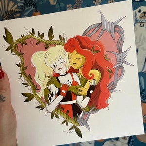 May include: A square print featuring two cartoon women embracing within a heart-shaped frame of vines. One woman has blonde hair and wears a black, red, and white outfit. The other has red hair and green skin. Barbed wire surrounds the heart.