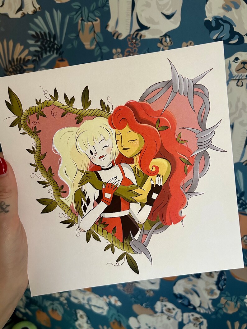 May include: A square print featuring two cartoon women embracing within a heart-shaped frame of vines. One woman has blonde hair and wears a black, red, and white outfit. The other has red hair and green skin. Barbed wire surrounds the heart.