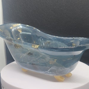 Peut inclure: Une petite baignoire en résine bleue avec des paillettes dorées. La baignoire a trois pieds et est posée sur une surface blanche.