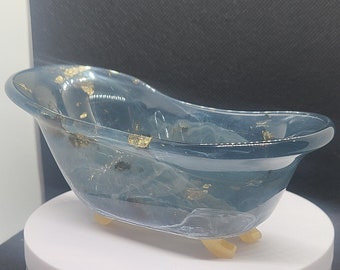 May include: A small, blue resin bathtub with gold flecks. The bathtub has three legs and is sitting on a white surface.