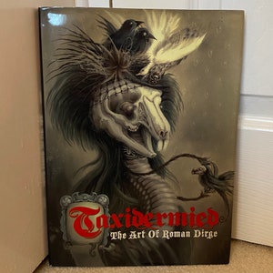 May include: A book cover with a dark background featuring a skeletal creature with a bird perched on its head. The title of the book is "Taxidermied: The Art of Roman Dirge".