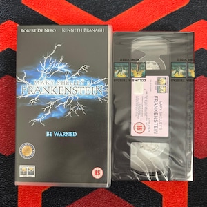 May include: A VHS tape of Mary Shelley's Frankenstein featuring Robert De Niro and Kenneth Branagh. The black case displays a blue lightning graphic and the text Be Warned. The tape itself is wrapped in plastic with a Columbia TriStar label.