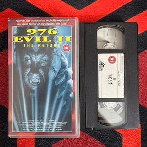 May include: A VHS tape and its plastic case for the film 976-EVIL II: THE RETURN. The cover features a blue-toned illustration of a monstrous face with sharp teeth and claws, an 18 age rating, and the text: Rarely has a sequel so perfectly captured.