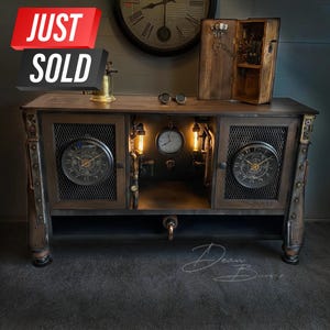 May include: A dark brown wooden cabinet with two doors and a shelf. The cabinet has a steampunk design with metal accents, gears, and clocks. The doors are open, revealing a shelf with a clock and a gauge. The cabinet is lit with small light bulbs.