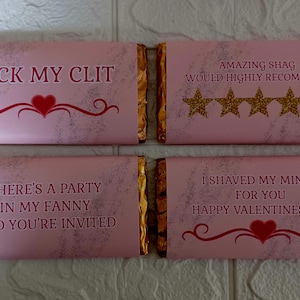 May include: Four pink chocolate bar wrappers with gold foil accents. The wrappers have humorous Valentine's Day themed messages printed on them. The first wrapper says "LICK MY CLIT" with a red heart. The second wrapper says "AMAZING SHAG WOULD HIGHLY RECOMMEND" with five gold stars. The third wrapper says "THERE'S A PARTY IN MY FANNY AND YOU'RE INVITED". The fourth wrapper says "I SHAVED MY MINGE FOR YOU HAPPY VALENTINES DAY!" with a red heart.