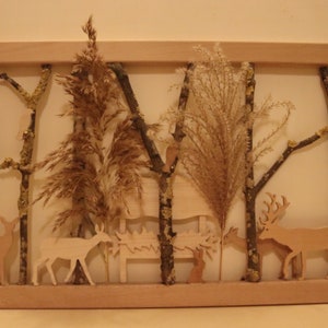 Puede incluir: Un marco de madera con un acabado de madera natural, que contiene una escena con temática de naturaleza. El marco está lleno de hierbas secas, ramitas y pequeñas figuritas de animales de madera, incluyendo ciervos y un conejo. La escena recuerda a un entorno de bosque.